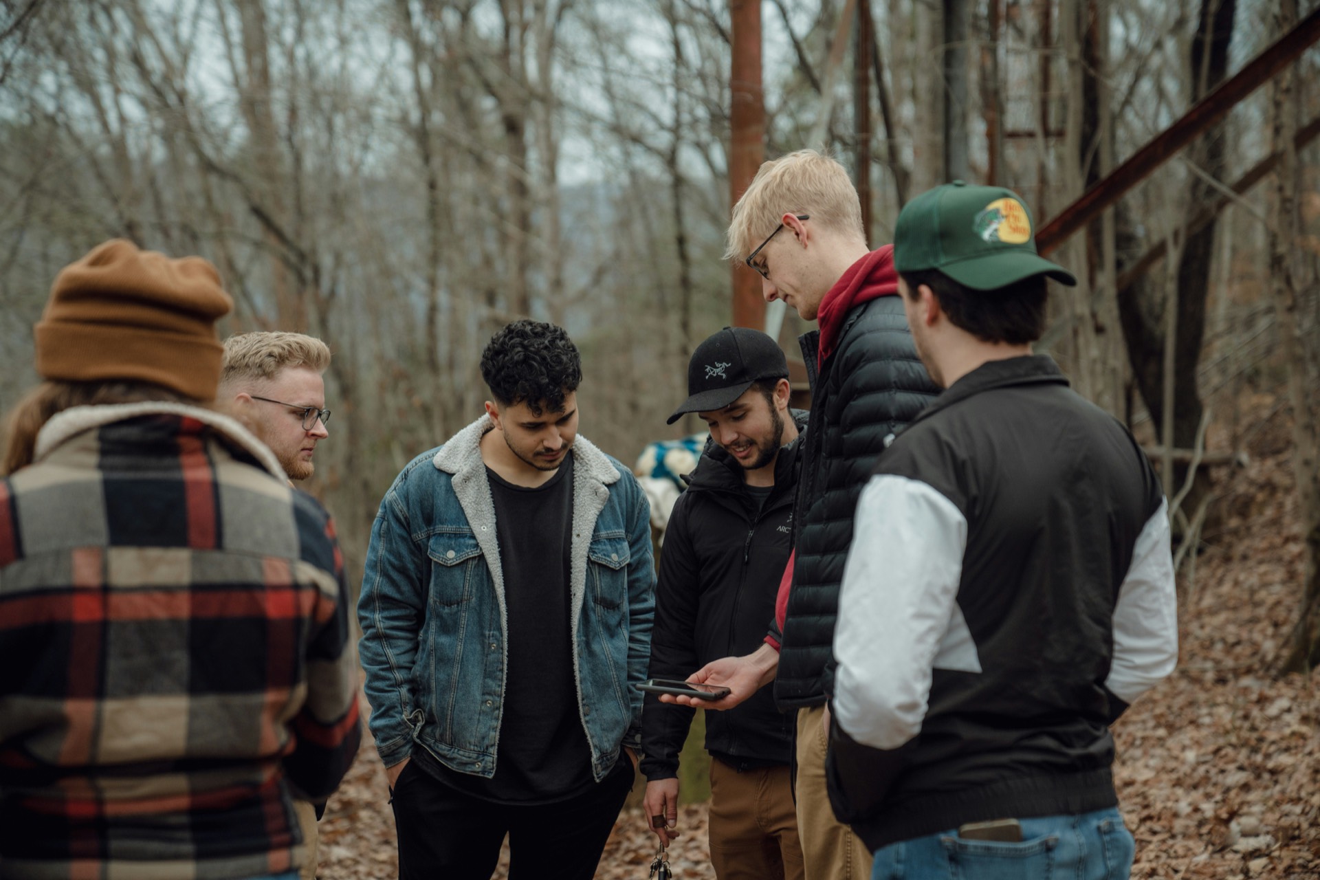 A small group of friends gathered around a phone on a woodland trail